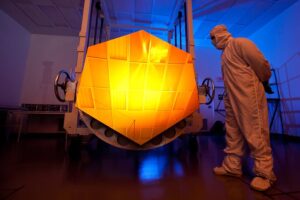 Inspection of a JWST Mirror panel within a dark clean-room shows the orange reflectance of the panel.