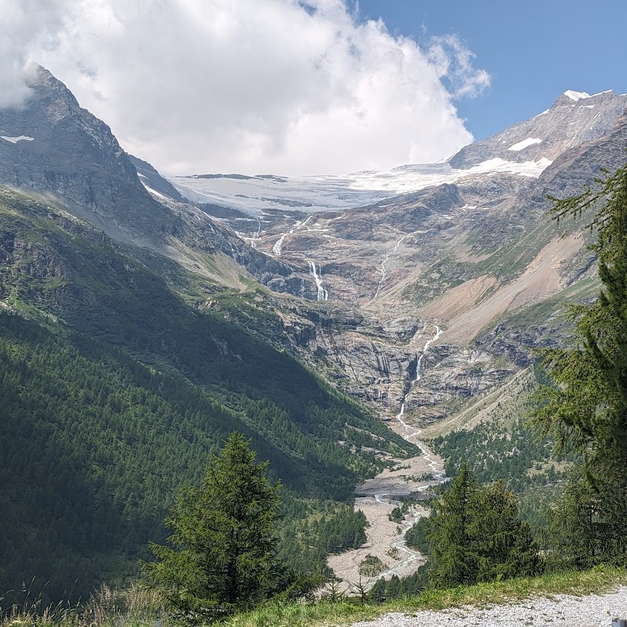 Glacier high in the Italian Alps surrounded by forest.